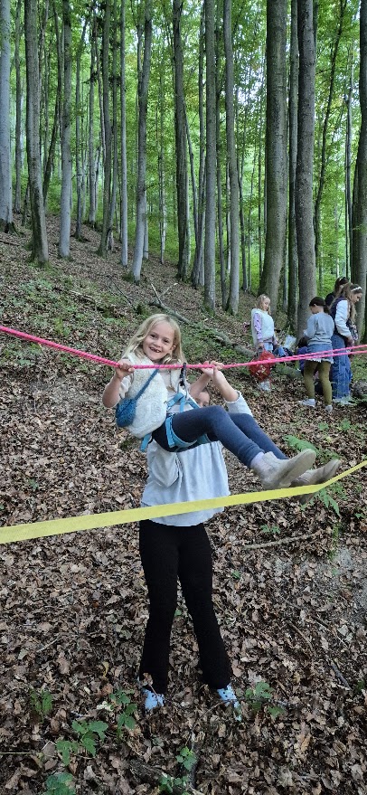 Ein Kind wird bei einer Mutprobe im Wald unter einem Absperrband hindurchgehoben.