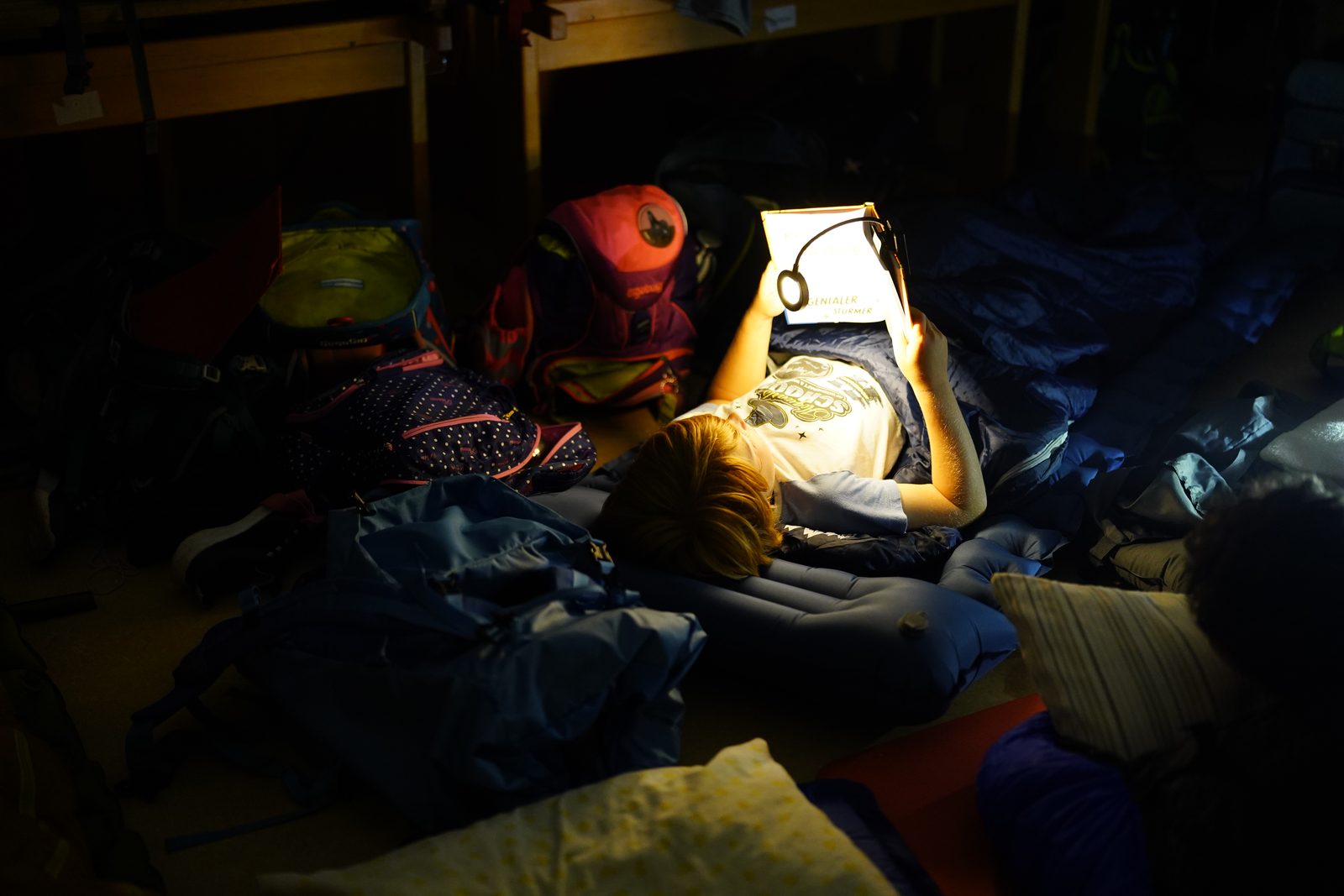 Kinder lesen am Abend in ihren Schlafsäcken bei Lampenlicht.